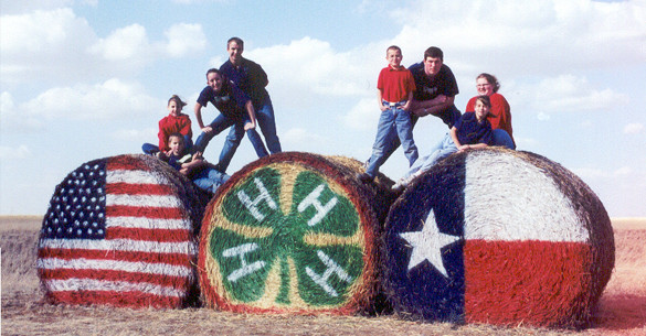 Students standing on 3 cotton bales decorated with the American flag, the 4-H clover logo, and the Texas flag